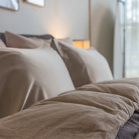 Detailed view of the head end of a plush bed with light filtering in from a large window featurin...