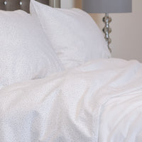 This image is a closeup view of soft, slighly tousled bedding with steel gray furnishings,  featu...