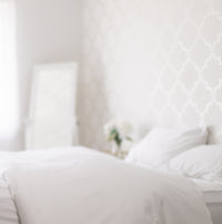 Photo of a beautiful white-on-white bedroom, with the focus on a bed in the foreground, white pat...
