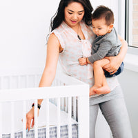 This image shows a woman holding a small child as she zips a QuickZip Crib sheet, showing the eas...