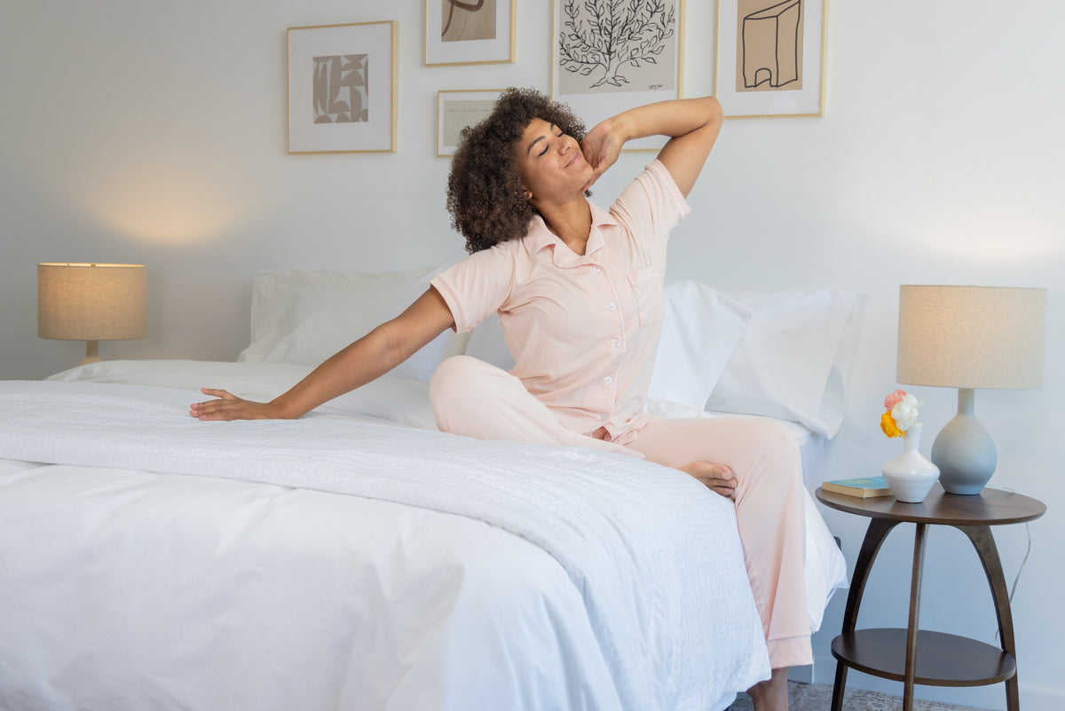 Woman stretching beside a bed dressed in white ComfortCore and Percale bedding