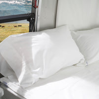 This image shows a corner of a bed in an Airstream RV trailer, with a mountain view out the windo...