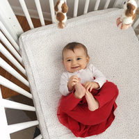 This image shows a child smiling and playing with her feet, laying on her back in a white crib. S...