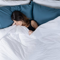 This photo shows a woman sleeping in comfort, reclining against two layers of pillows and underne...
